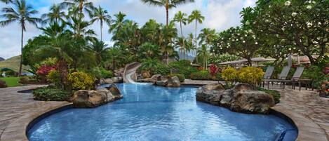 A swimming pool with a water slide, surrounded by palm trees and tropical plants.