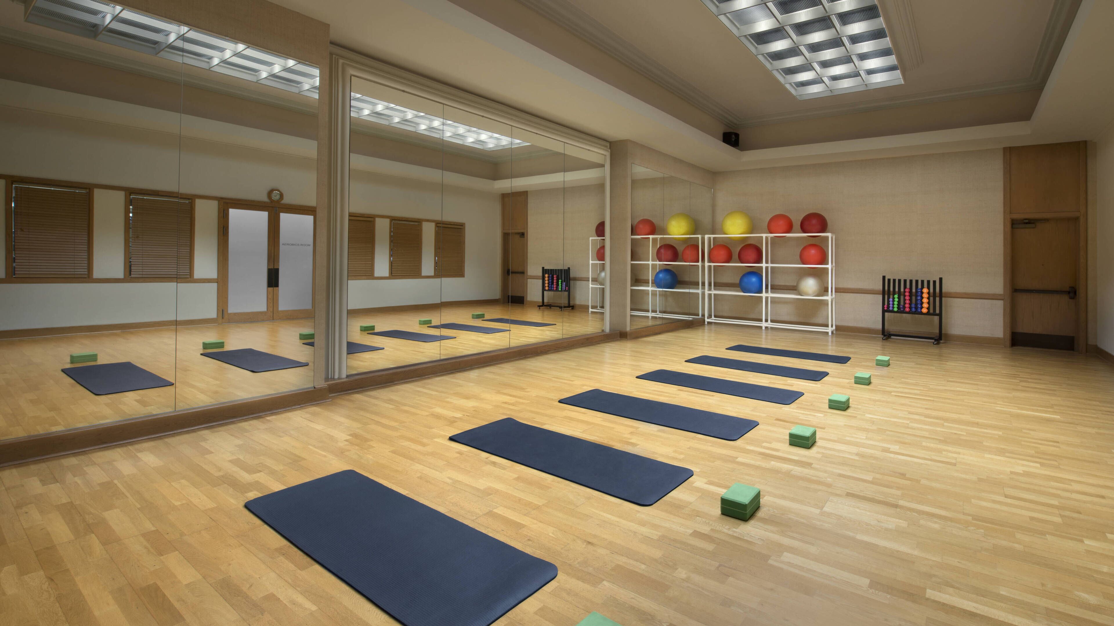 Une pièce spacieuse dotée d’un grand miroir, d’un plancher en bois et de tapis de sol disposés pour la pratique du yoga ou des exercices d’étirement.