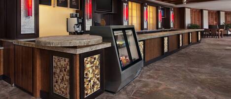 A modern bar area with a stone countertop, a coffee machine, and a menu board displaying various drink options.