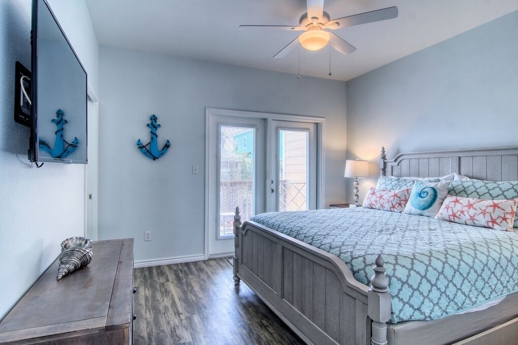 A bedroom with a bed, a ceiling fan, a wooden nightstand, and a door leading to a balcony.