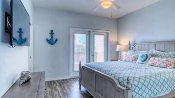 A bedroom with a bed, a ceiling fan, a wooden nightstand, and a door leading to a balcony.