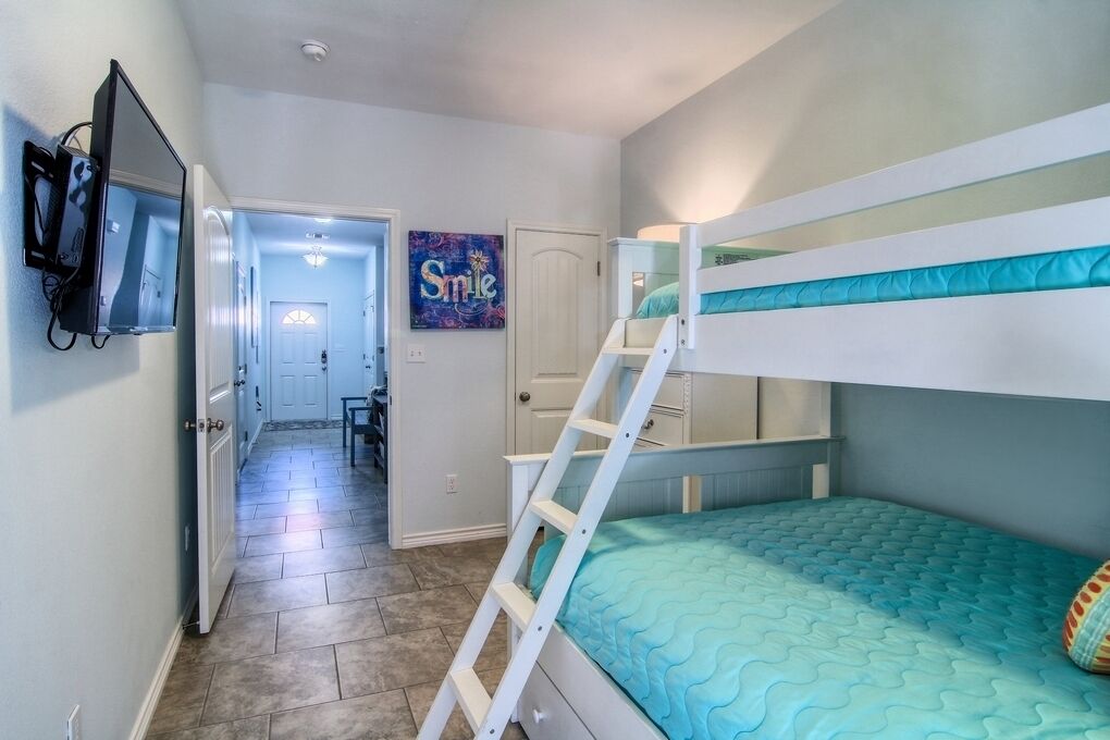 A bunk bed room with a ladder, a door leading to another room, and a wall-mounted TV.