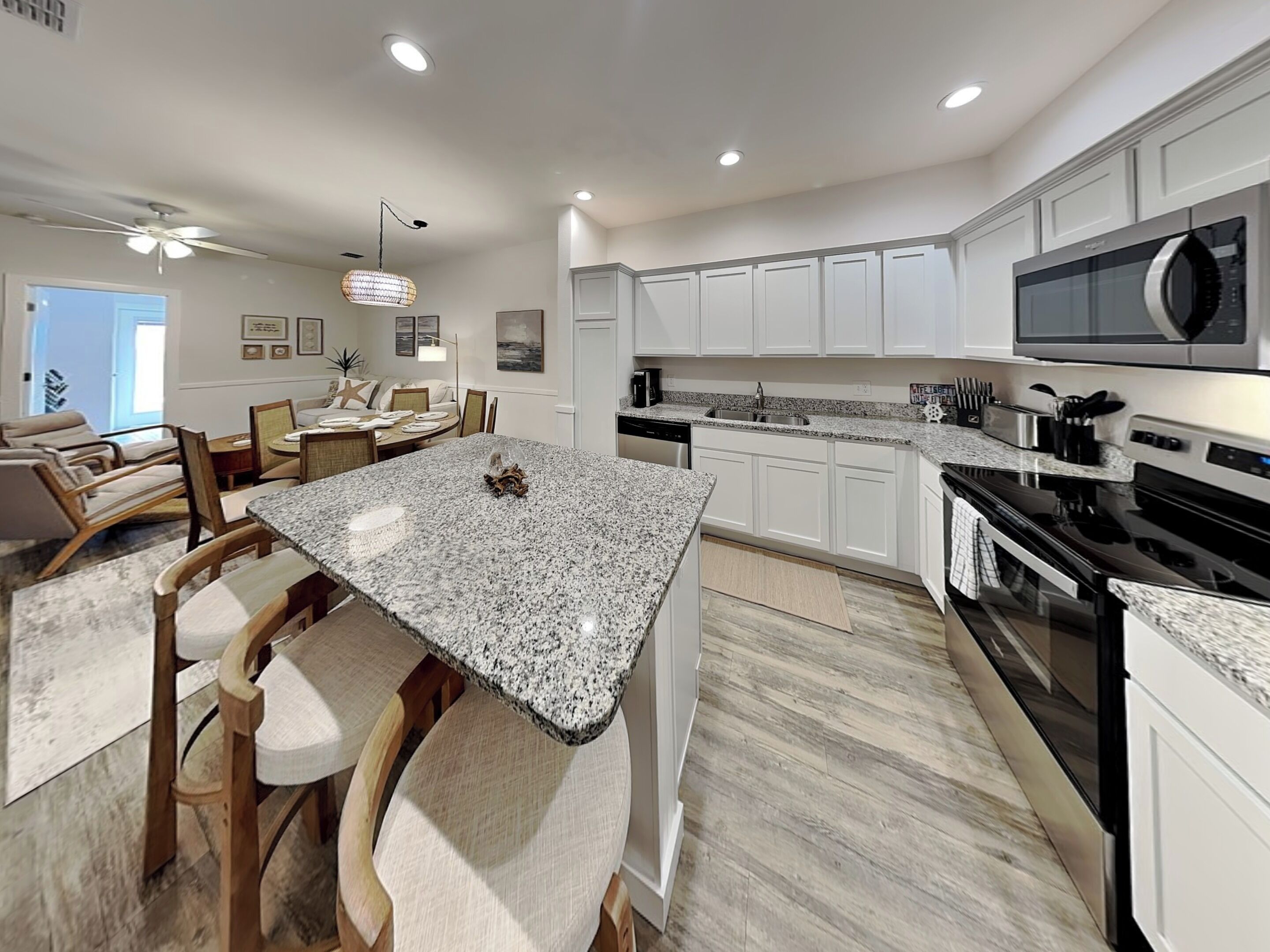 A modern kitchen with granite countertops, white cabinetry, a built-in microwave, and a dining area with a round table and chairs.