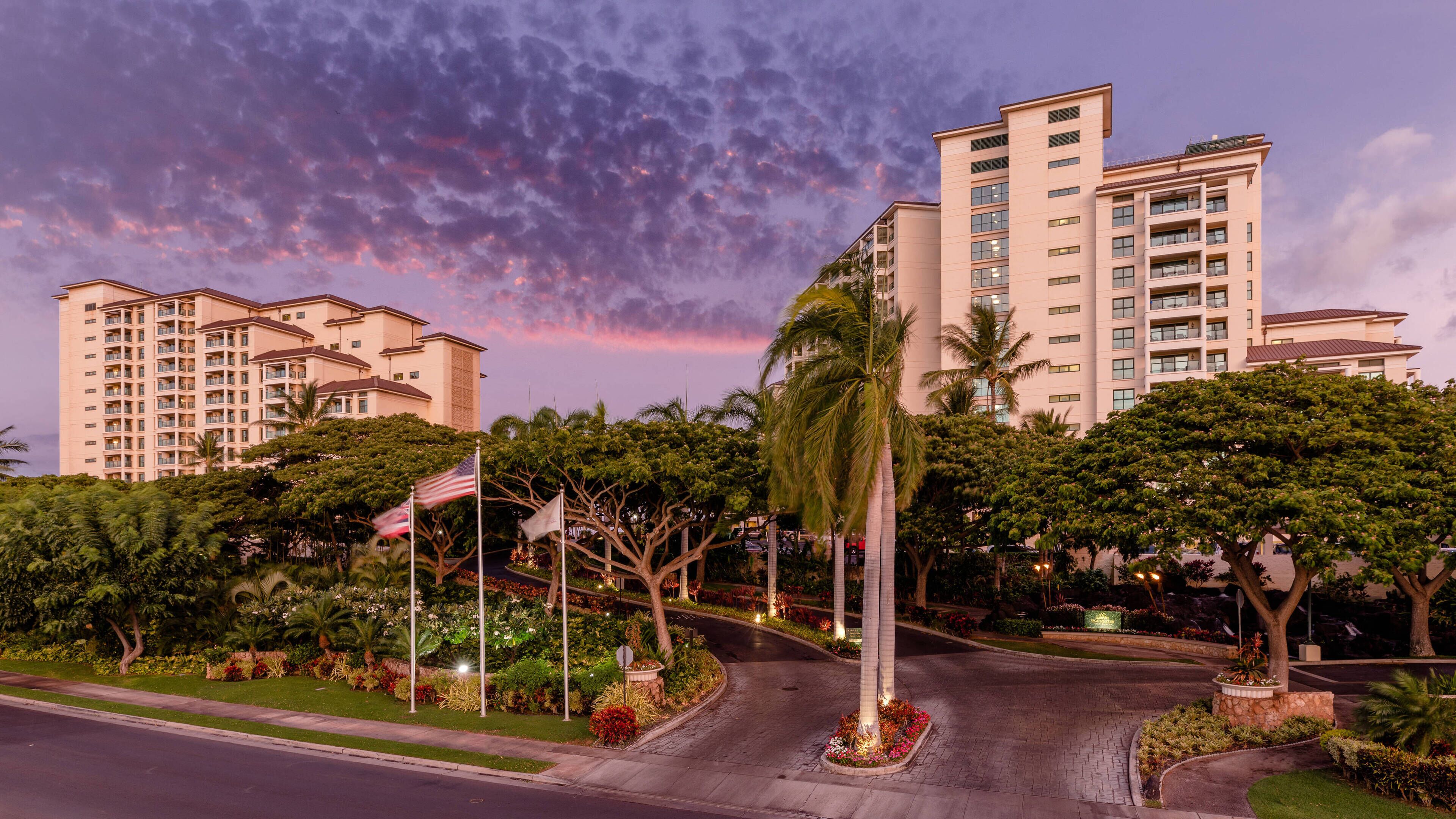 A multi-story hotel with a landscaped entrance, palm trees, and a flag.