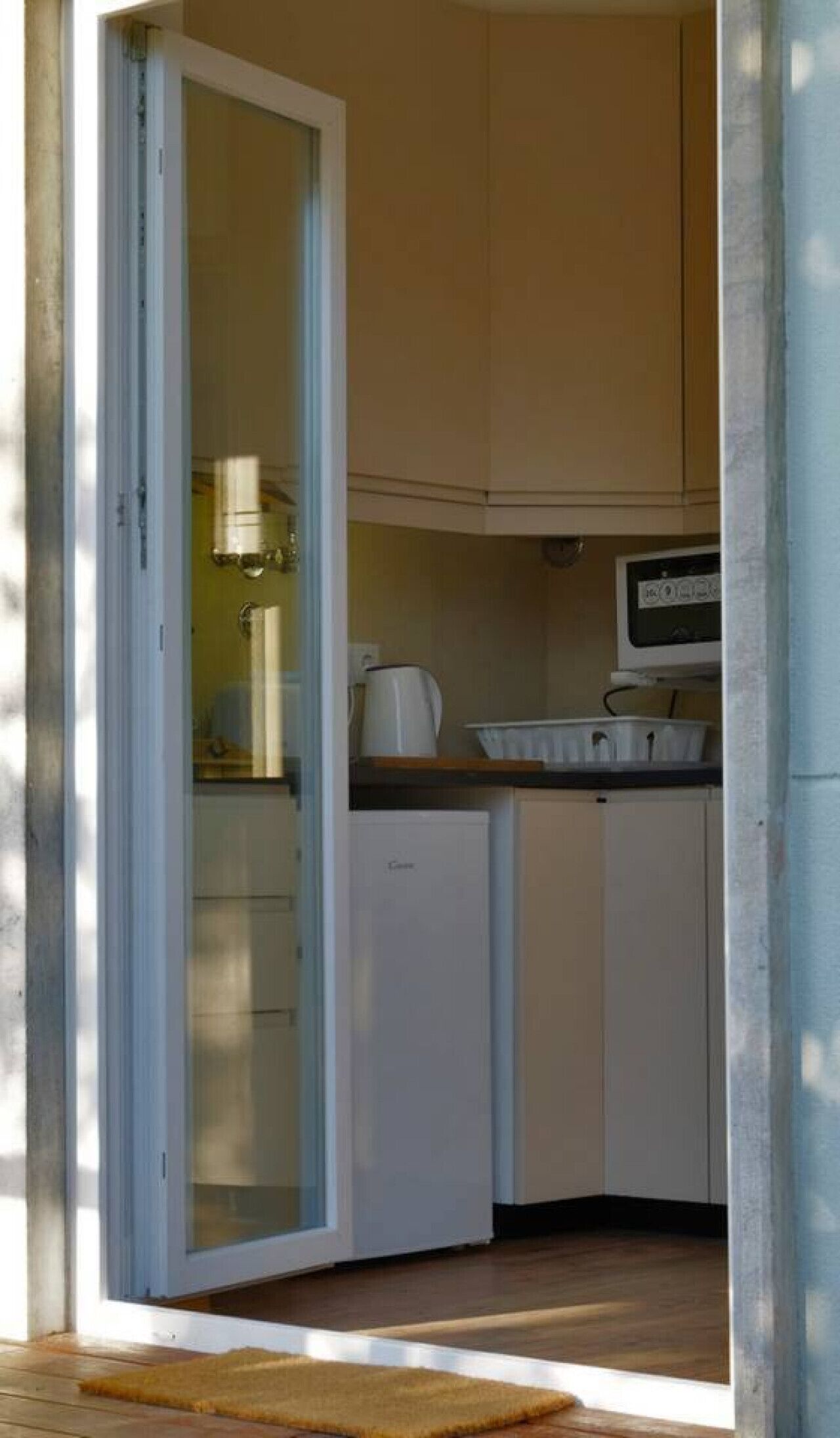 Cocina compacta con nevera, microondas y hervidor sobre la encimera.