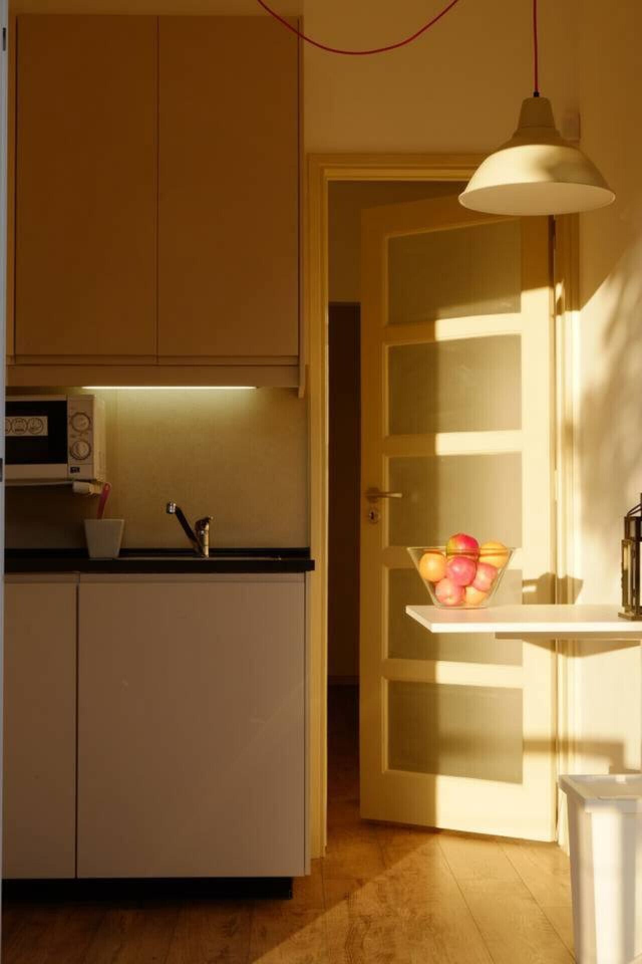 Une cuisine équipée d’un four à micro-ondes, d’un évier et d’un saladier rempli de fruits, posé sur une petite table.