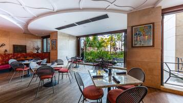 A modern restaurant with a mix of booth and table seating, a view of tropical plants, and a large painting on the wall.
