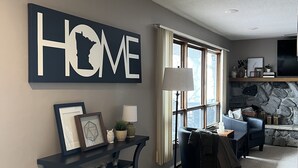 A living room with a large 'HOME' sign, a dark console table with decorative items, a blue sofa, and a stone fireplace.
