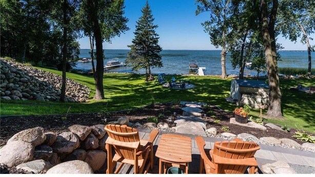 A patio with wooden furniture, a stone wall, and a view of the water.