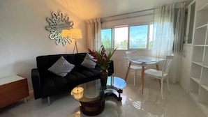Una sala de estar moderna con un sofá negro, una mesa de centro de vidrio y un comedor con una mesa de vidrio y sillas blancas.