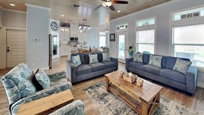 A spacious living room with a grey sofa set, a coffee table, and a patterned rug. - Postcard from Paradise by Silver Sands Vacation Rentals (Port Aransas)