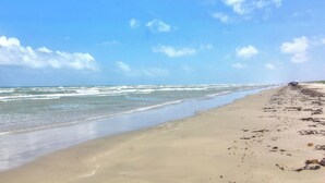 A beach with a clear sky, waves, and a distant figure. - Postcard from Paradise by Silver Sands Vacation Rentals (Port Aransas)