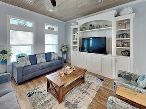 A living room with a grey sofa, wooden coffee table, and a TV on a white cabinet.