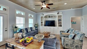 A spacious living room with a wooden ceiling, a large TV, and a dining area with a wooden table and chairs. - Postcard from Paradise by Silver Sands Vacation Rentals (Port Aransas)