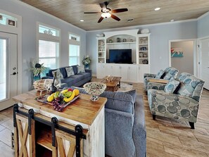 A spacious living room with a wooden ceiling, a large TV, and a dining area with a wooden table and chairs.