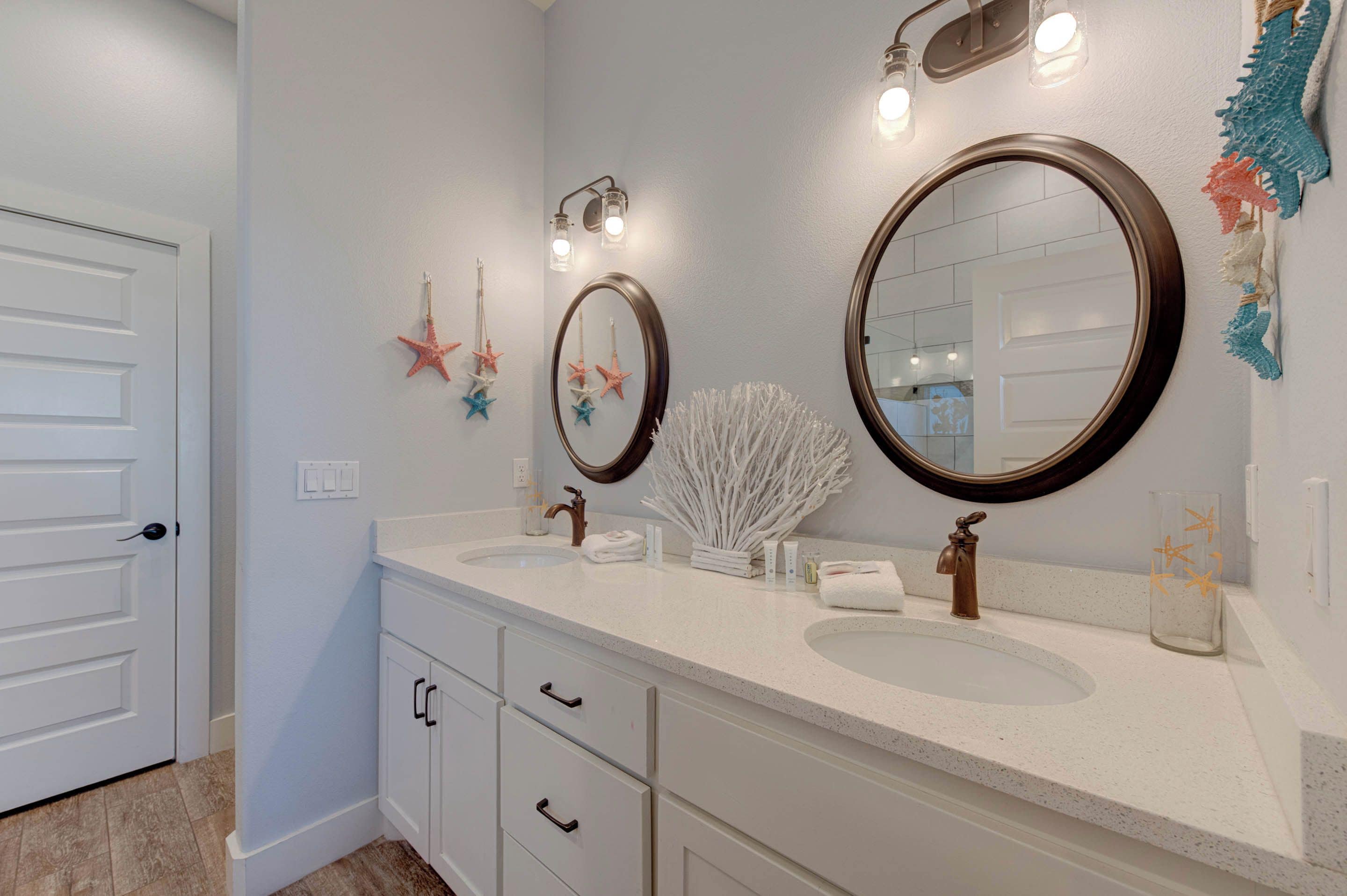 Un baño con dos lavabos, un espejo y estrellas de mar decorativas. Hay apliques de pared y una puerta con manija.