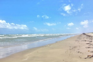 A beach with a clear sky, waves, and a distant figure.