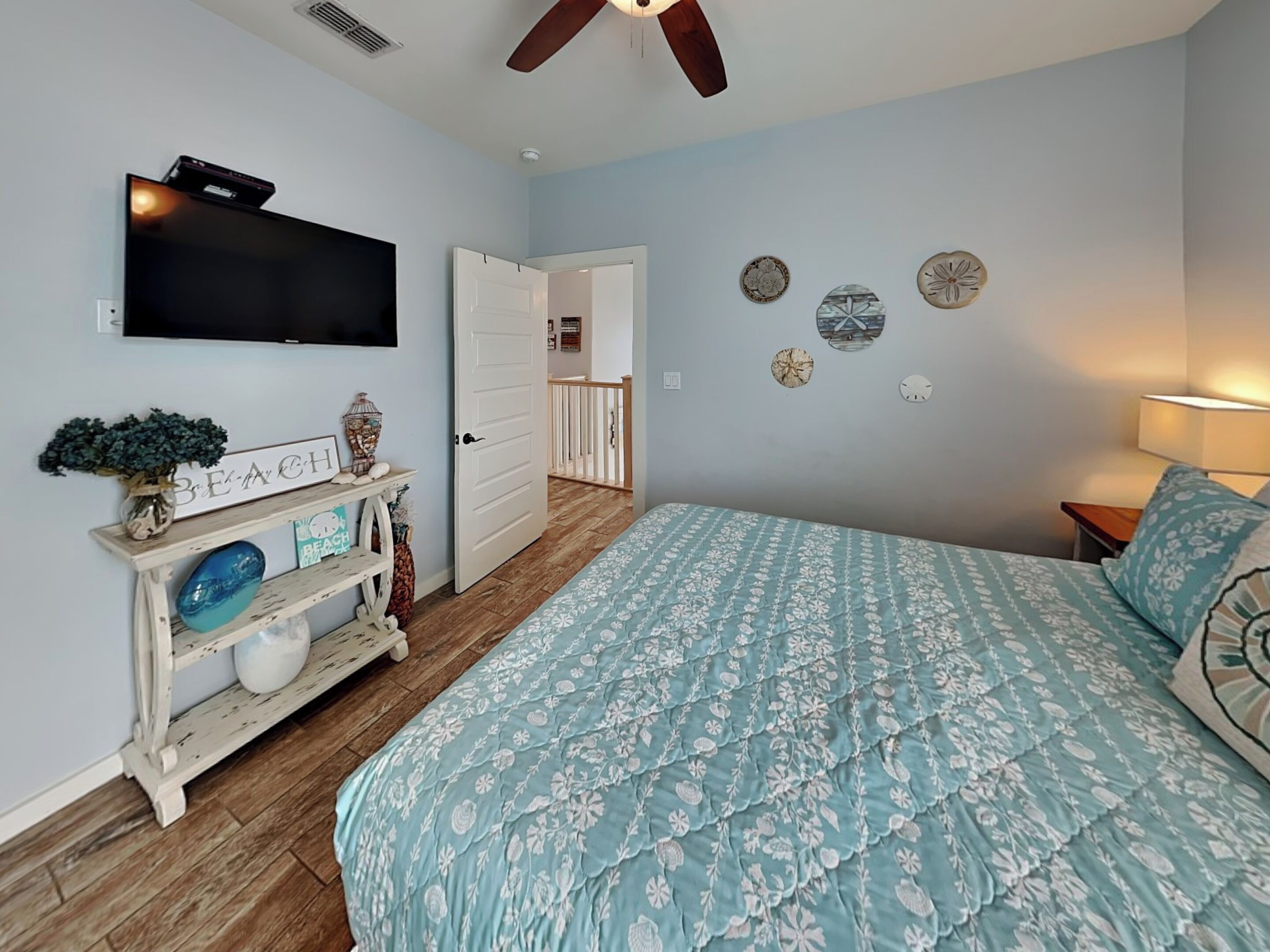 A bedroom with a bed, a TV, a console table with decorative items, a door leading to a balcony, and wall decor.