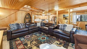 Ein gemütliches Blockhaus-Interieur mit einer großen L-förmigen Ledersofa, einem gemusterten Teppich, Holzwänden und einer Küchenzeile.