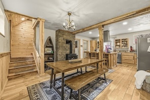 A wooden interior with a dining table, benches, a fireplace, and a kitchen area.