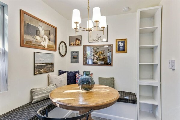 A dining area with a round wooden table, a bench, and a chandelier.
