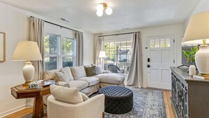 A living room with a sectional sofa, a round ottoman, a side table, and a lamp. - The Mountainside Cottage | Backyard | BBQ (Provo)