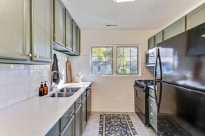 A kitchen with light green cabinets, a stainless steel refrigerator, a gas stove, and a window providing natural light. - The Mountainside Cottage | Backyard | BBQ (Provo)