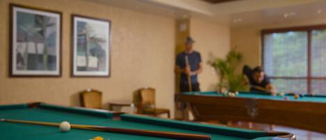 A pool table with balls, a cue stick, and two framed pictures on the wall.