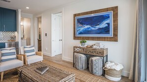 A living room with a large abstract painting, wicker furniture, and a console table with decorative items. - The Sanctuary by Silver Sands Vacation Rentals (Port Aransas)