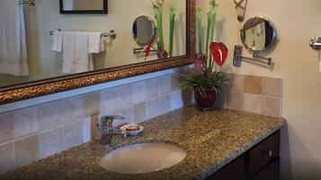 A bathroom with a granite countertop, a white sink, two round mirrors, a potted plant, and a towel rack with a white towel.