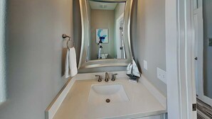 A bathroom with a white sink, two faucets, a mirror, and a towel rack. - All Decked Out by Silver Sands Vacation Rentals (Port Aransas)