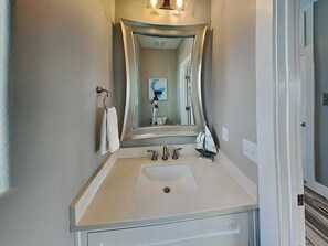 A bathroom with a white sink, two faucets, a mirror, and a towel rack. - All Decked Out by Silver Sands Vacation Rentals (Port Aransas)