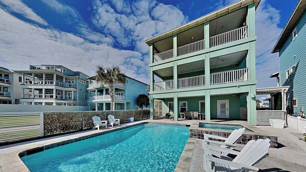 A swimming pool with lounge chairs, a multi-story building with balconies, and a clear sky. - All Decked Out by Silver Sands Vacation Rentals (Port Aransas)