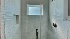 A glass-enclosed shower with a handrail, a small window, and a metallic door handle. - All Decked Out by Silver Sands Vacation Rentals (Port Aransas)