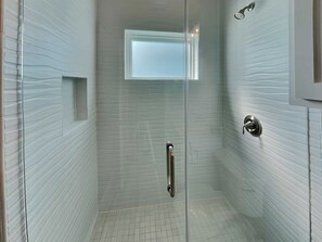 A glass-enclosed shower with a handrail, a small window, and a metallic door handle. - All Decked Out by Silver Sands Vacation Rentals (Port Aransas)
