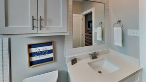 A bathroom with a white sink, a mirror, and a framed sign that reads 'STAY while.' - All Decked Out by Silver Sands Vacation Rentals (Port Aransas)