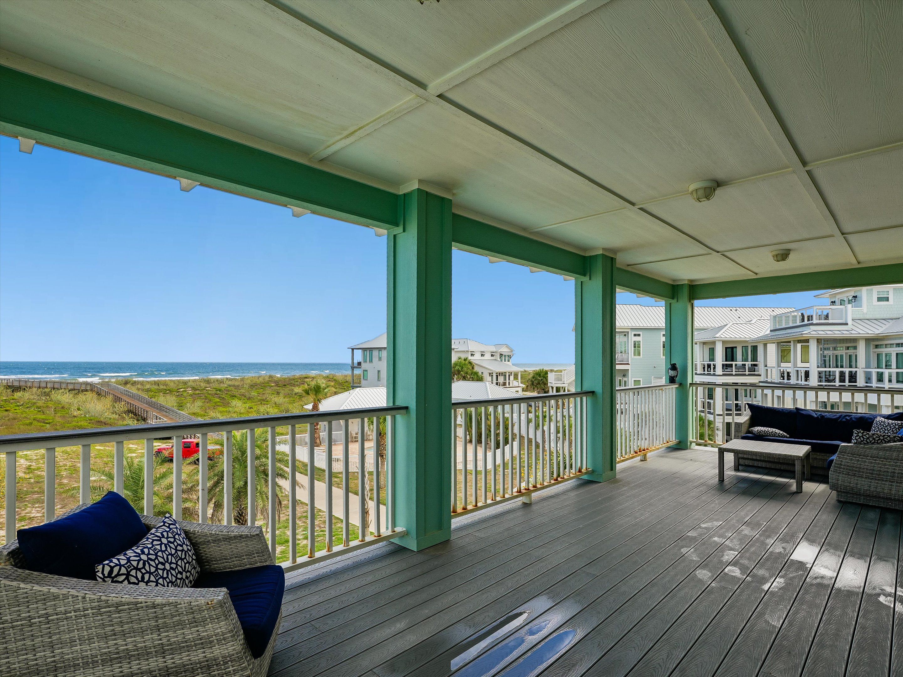 A covered outdoor area with a view of the beach, wooden flooring, and outdoor furniture.
