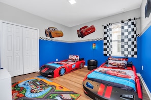 Ein Kinderzimmer mit zwei Betten, Rennwagen-Bettwäsche und einem Rennstrecken-Teppich.