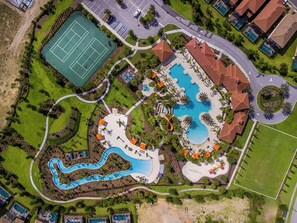 Luftaufnahme eines Resorts mit Schwimmbad, Tennisplatz und angelegten Grünflächen.