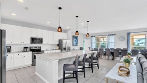 A modern kitchen with white cabinets, a central island with bar stools, and pendant lighting. - Solterra Escape | 14 Bdr, Game Room, Lego Playroom, Theater, Private Pool (Davenport)