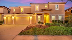 A two-story house with a garage, a well-maintained lawn, and a small tree in front. - Solterra Escape | 14 Bdr, Game Room, Lego Playroom, Theater, Private Pool (Davenport)