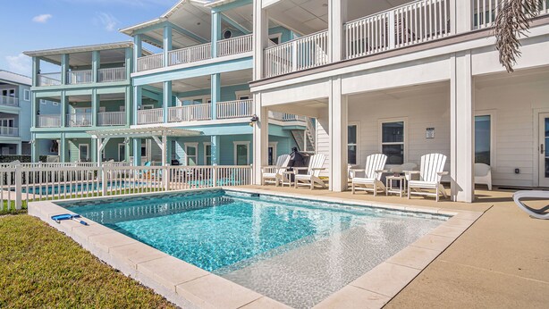 A multi-story building with a pool area featuring a white fence, lounge chairs, and a clear blue pool.