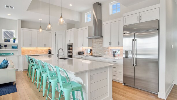 A modern kitchen with white cabinetry, a stainless steel refrigerator, and a central island with bar stools. - The White House by Silver Sands Vacation Rentals (Port Aransas)