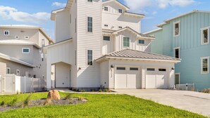 A multi-story residential building with a garage, a well-maintained lawn, and a clear sky. - The White House by Silver Sands Vacation Rentals (Port Aransas)