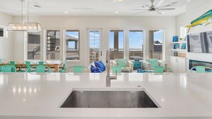 A spacious kitchen with a central island, large windows, and a ceiling fan. - The White House by Silver Sands Vacation Rentals (Port Aransas)