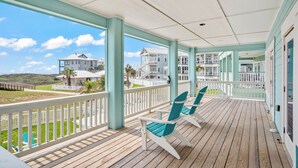 A wooden deck with two turquoise Adirondack chairs, a white railing, and a view of beachfront houses. - Beach-A-Holic by Silver Sands Vacation Rentals (Port Aransas)