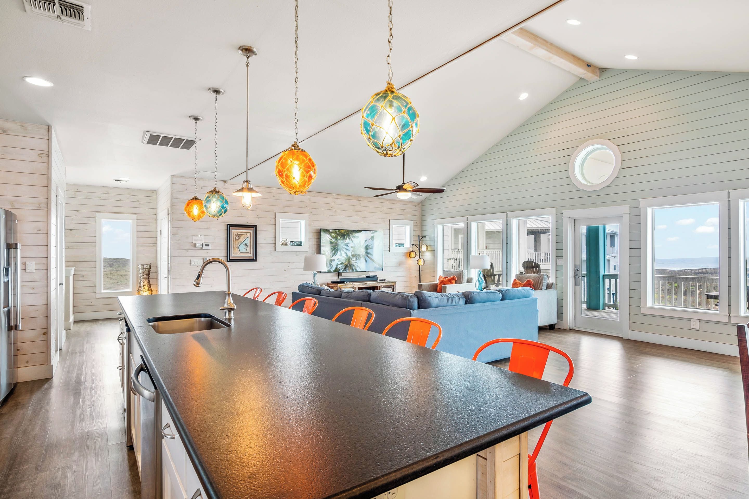 A spacious kitchen with a large island, bright pendant lights, and a view to the living area.