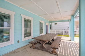 A covered patio with a wooden table and benches, light blue siding, and white trim.