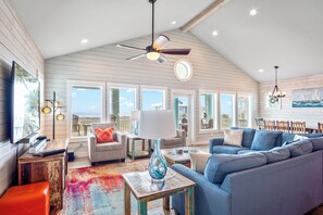 Un salon spacieux avec un plafond haut, de grandes fenêtres, un ventilateur de plafond et un tapis aux couleurs vives.