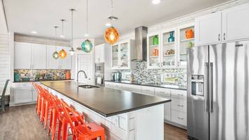 A modern kitchen with white cabinets, a stainless steel refrigerator, and a long island with orange stools.